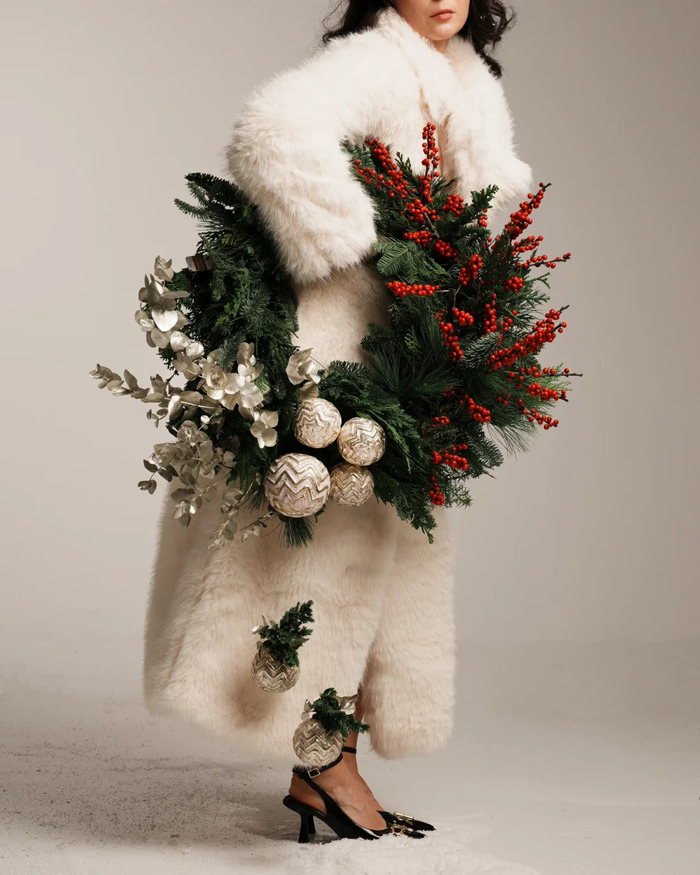 Woman holding an evergreen Christmas wreath decorated with red berries, metallic foliage and gold ornaments