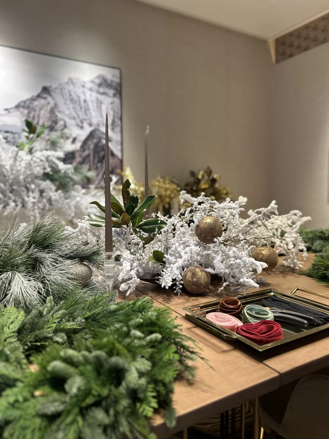 Evergreen foliage and snow-covered branches with gold ornaments, taper candles and ribbons on a wooden table