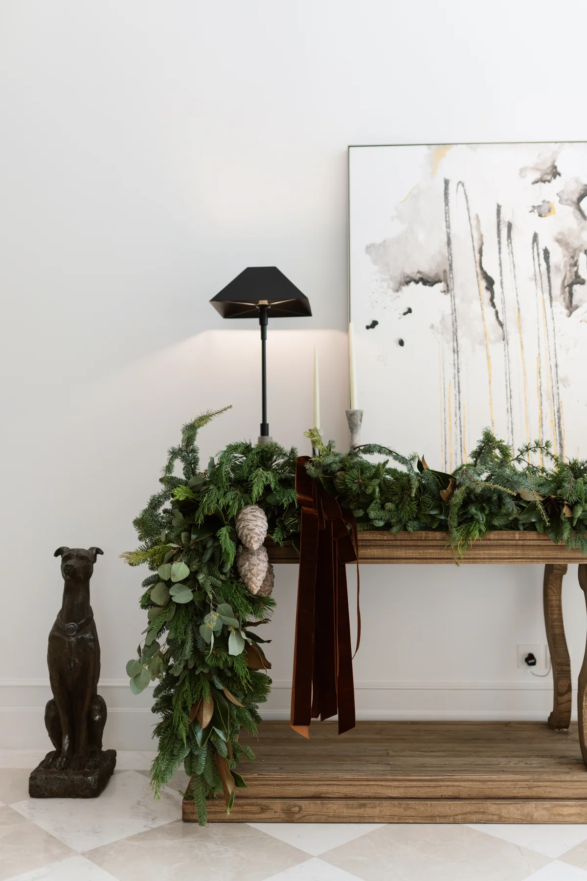 Christmas garland of evergreen foliage, eucalyptus and pine cones with burgundy velvet ribbons draped over a wooden console table