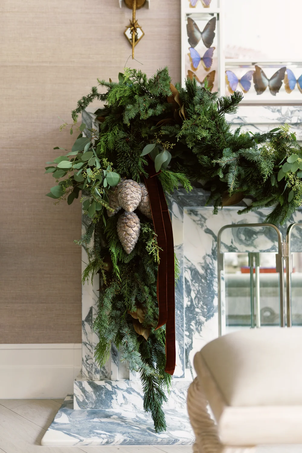 Evergreen Christmas garland with eucalyptus, pine cones and burgundy ribbons draped across a marble fireplace